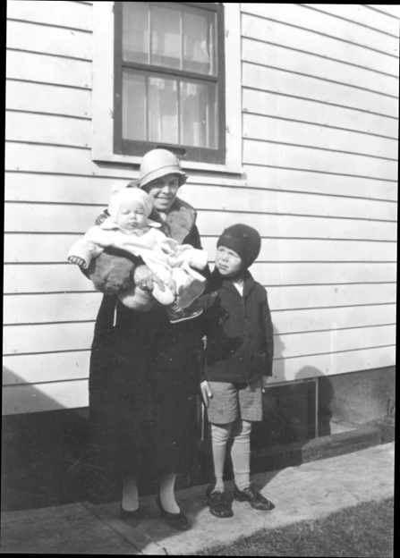 A photograph of a mother holding a baby while a small boy stands next to her.