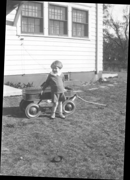 A little boy stands by a four-wheel cart in the backyard.