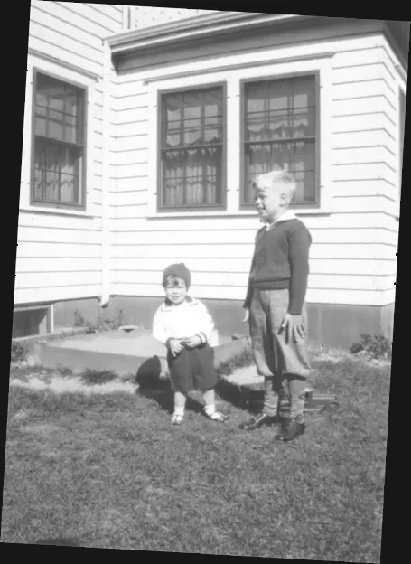 A photograph of two boys standing in the back yard, Bill looks at the camera.