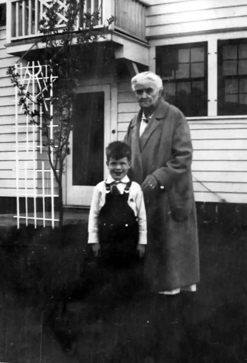 A photograph of a young boy with a coat-wearing Grandma standing in the back yard.