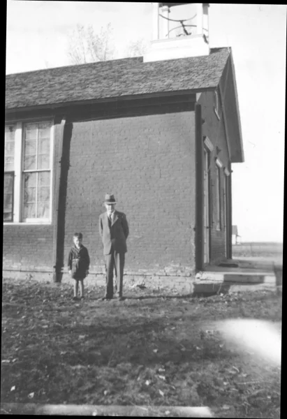 A photograph of a young boy and his aunt in winter clothes, standing on the step at the back door.
