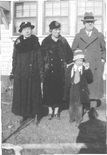 A photograph of a boy, his grandmother, his aunt, and his father all in winter clothing, standing in the backyard.