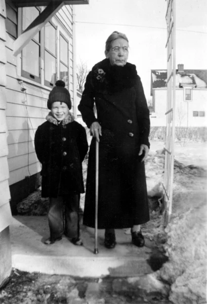 A photograph of a boy and his aunt in winter clothing, standing on the step at the back door.