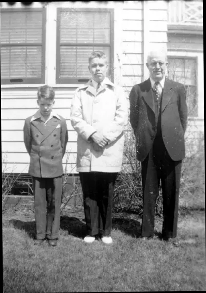 A photograph of two boys and their father standing in the backyard, the guy in the middle is wearing a raincoat maybe.