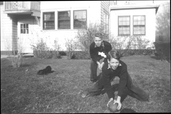 A photograph of two boys playing with a football in the backyard.