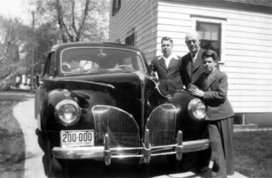 A photograph of a man and his two sons all in suits stand next to a new MY1941 Lincoln in the driveway.