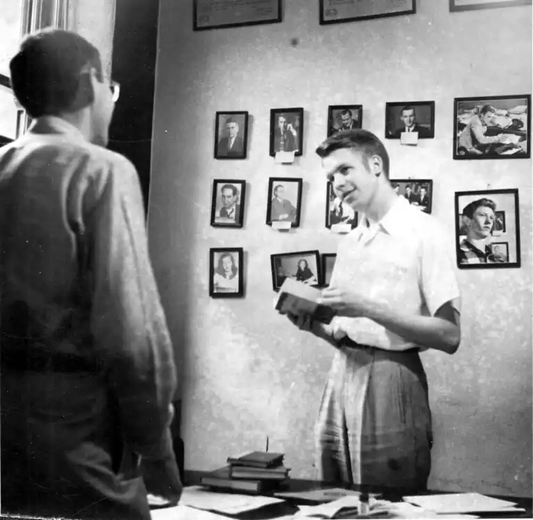 A photograph of reporter Bill Hannaher with framed photographs on the wall behind him.