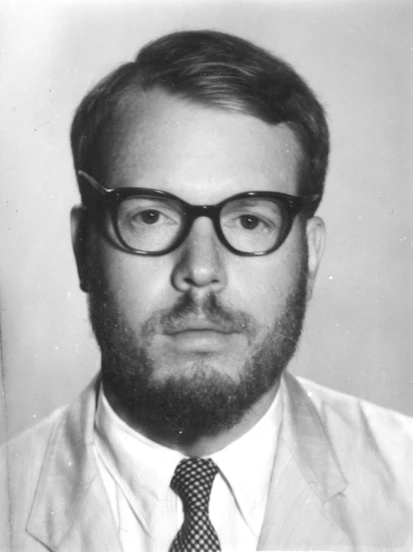 A photograph of a bearded white man wearing glasses, a suit, and a tie.