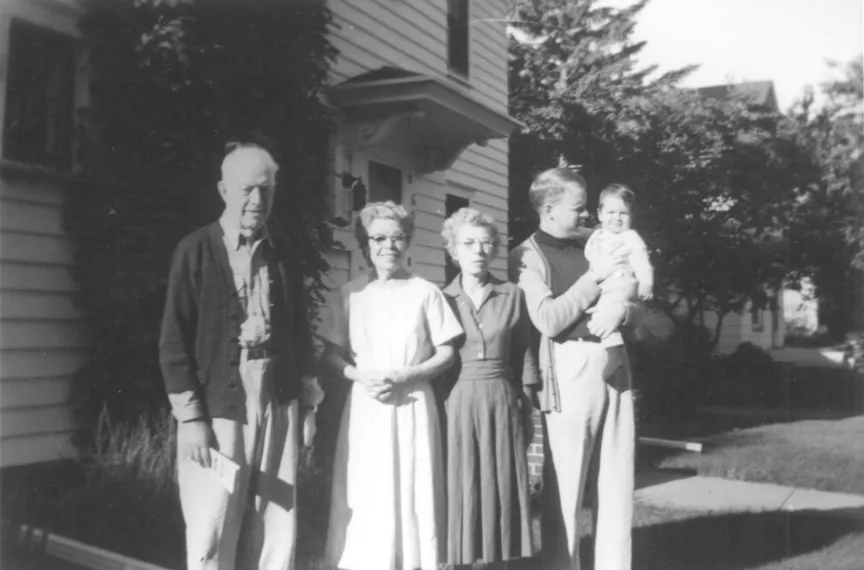 A photograph of a grandfather, a grandmother, her sister, and a red-haired man with a son in front of the family house.