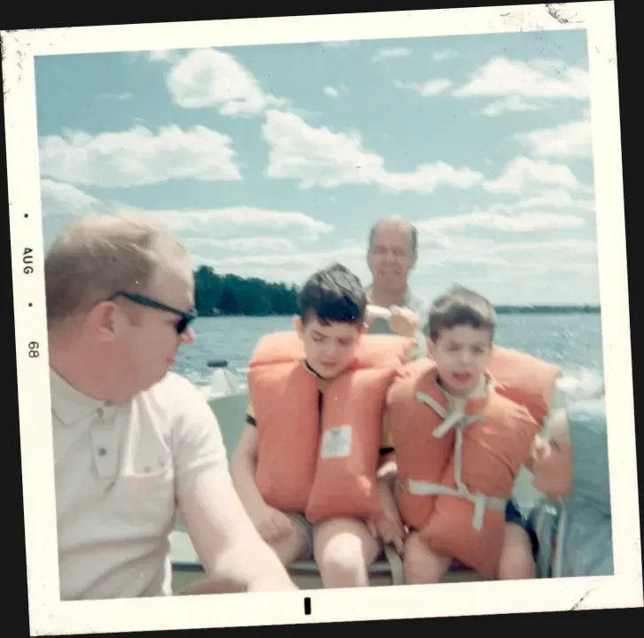 A photograph of two men and two boys in life preservers all in a boat, the men are brothers, too.