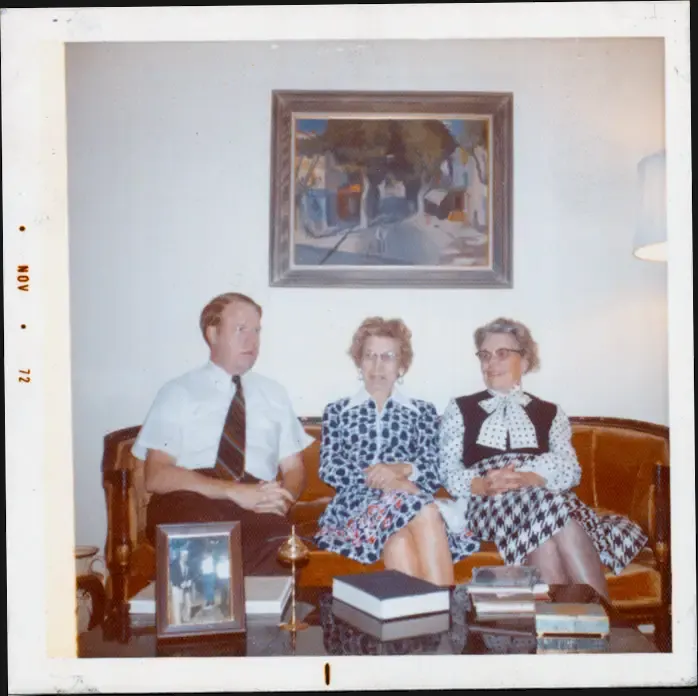 A photograph of a men and his mother and his aunt, sitting on a sofa with gold-colored cushions.