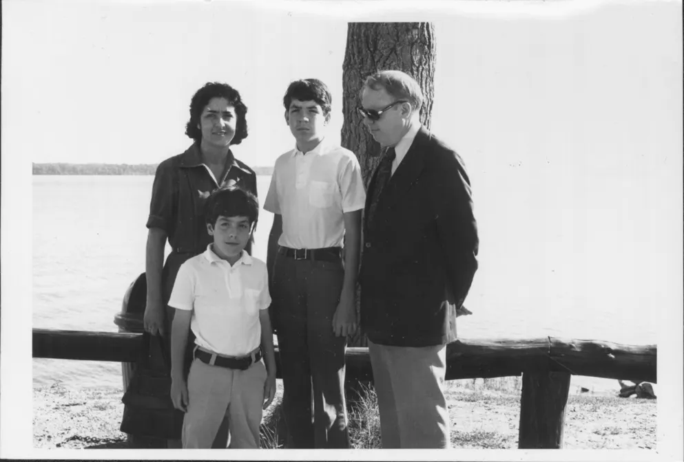 A photograph of a family on a river shore by a tree, the father does not look at the camera.